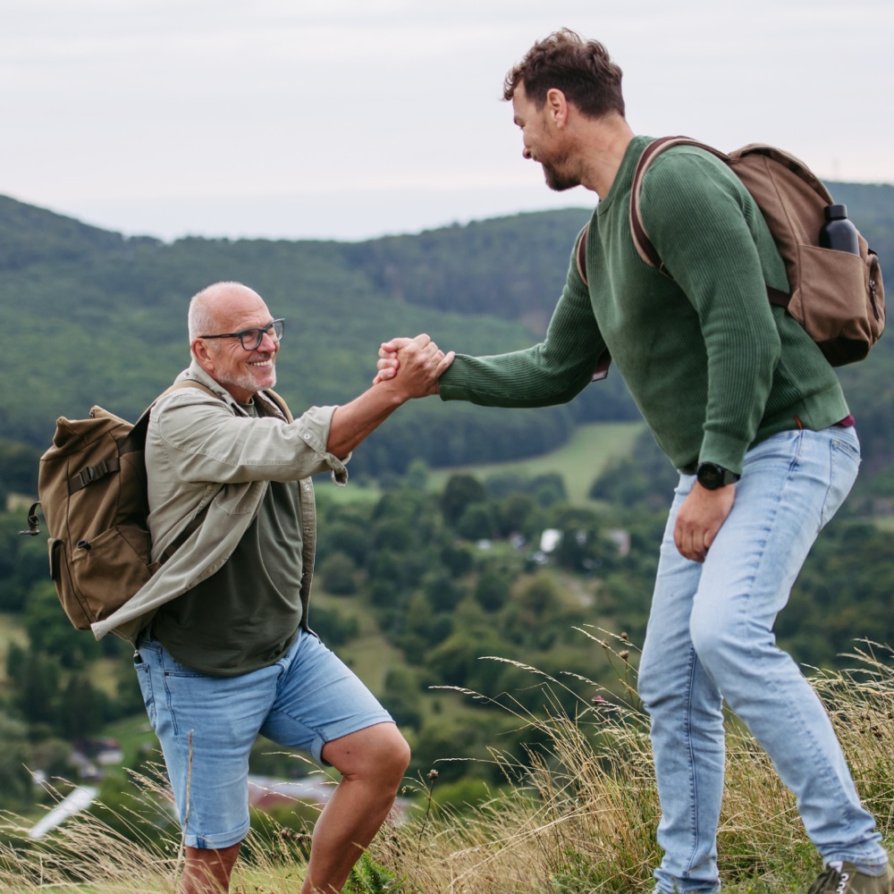 A younger man helping an older man up a grassy hillside